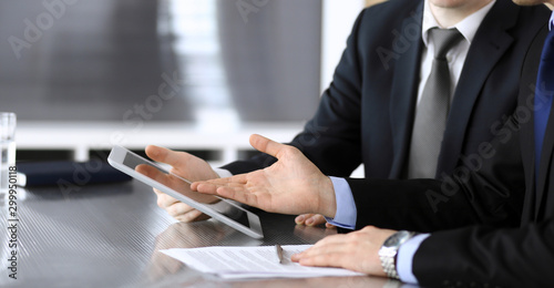 Businessman using tablet computer and work together with his colleague or partner at the glass desk in modern office, close-up. Unknown business people at meeting. Teamwork and partnership concept
