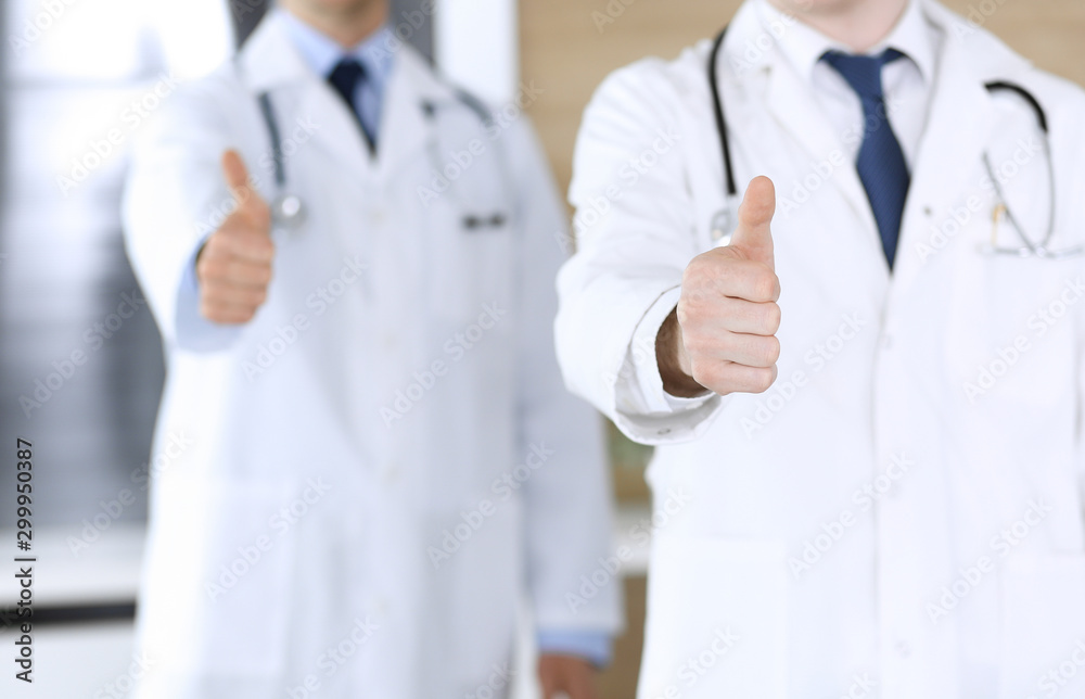 Group of modern doctors standing as a team with thumbs up or Ok sign in hospital office, close-up. Physicians ready to examine and help patients. Medical help, insurance in health care, best treatment Group of modern doctors standing as a team with thumbs up or Ok sign in hospital office, close-up. Physicians ready to examine and help patients. Medical help, insurance in health care, best treatment