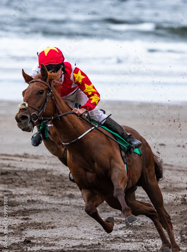 Lead race horse and jockey galloping at speed on the beach
