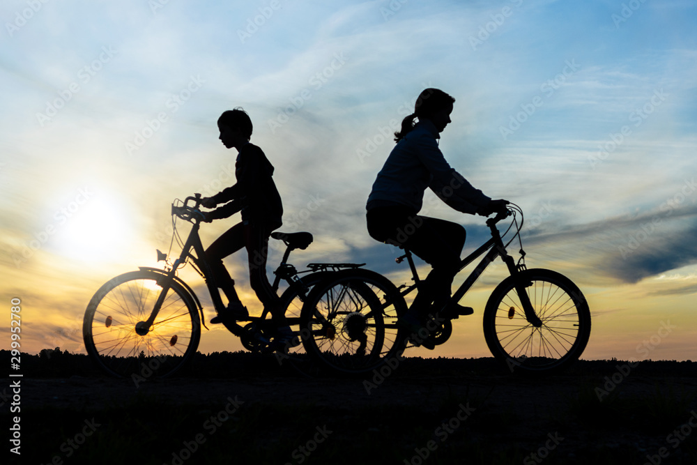 Obraz premium Boy and young girl riding bikes in different directions, silhouettes of riding persons at sunset in nature