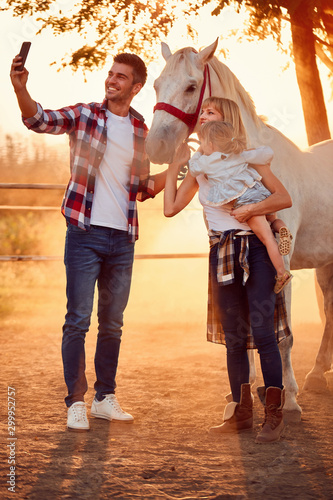  Smiling family make selfie with a beautiful horse on the countryside .