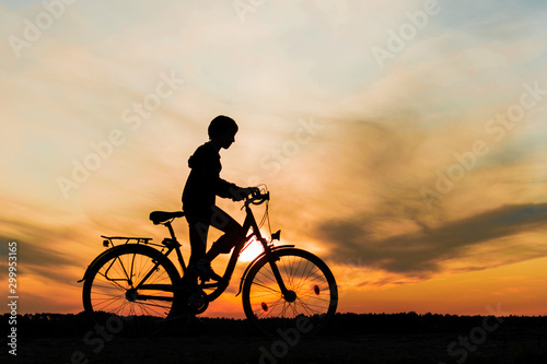 Boy , kid 10 years old riding bike in countryside, silhouette of riding person at sunset in nature