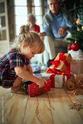 girl open present in front of a decorated Christmas tree