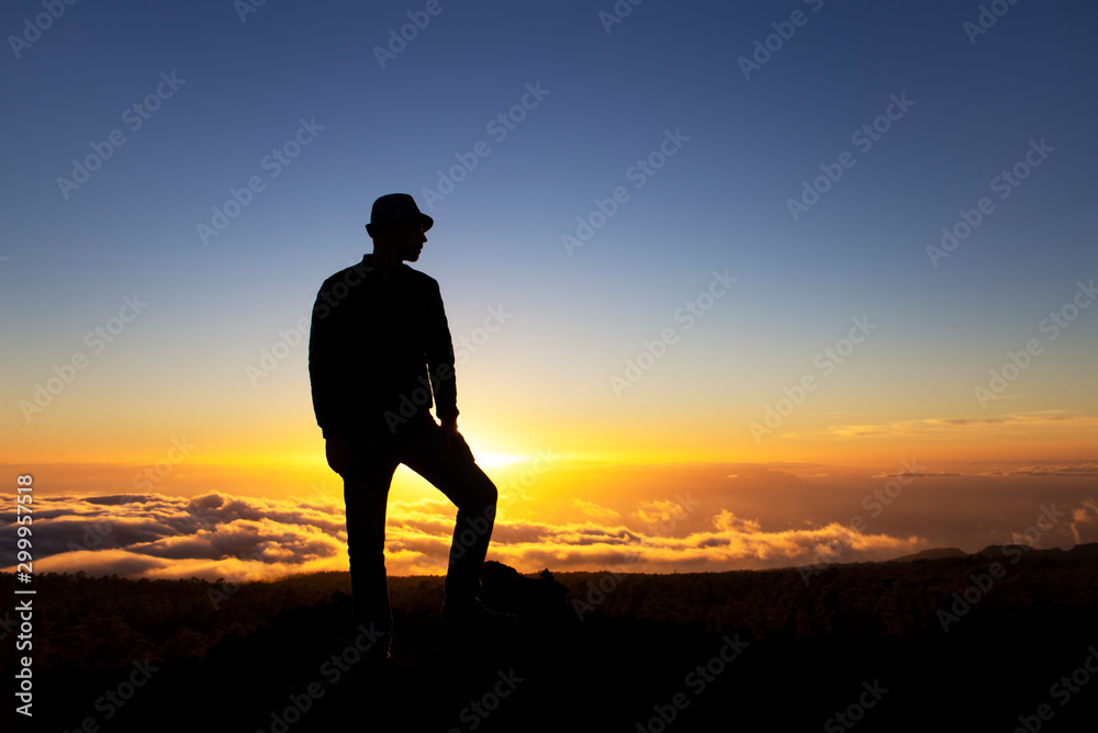 Man leader stands on a mountain at sunset high above clouds. Success and conquest of peaks, aspiration to be first. A man who achieved his goals. Climb mountain, be higher and more successful than all