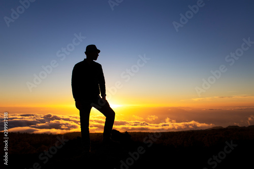 Man leader stands on a mountain at sunset high above clouds. Success and conquest of peaks, aspiration to be first. A man who achieved his goals. Climb mountain, be higher and more successful than all