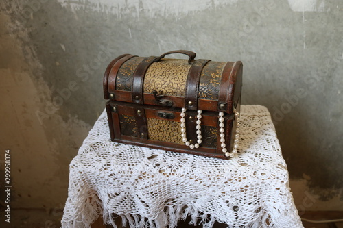 Photography Closed dusty beautiful brown chest on a white knitted tablecloth against the concrete gray streaked wall