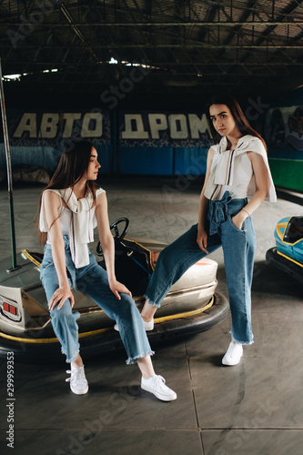 Portrait of Two Young Brunette Twins Sisters Dressed Alike in Jeans and White T-shirt, Posing on Racetrack