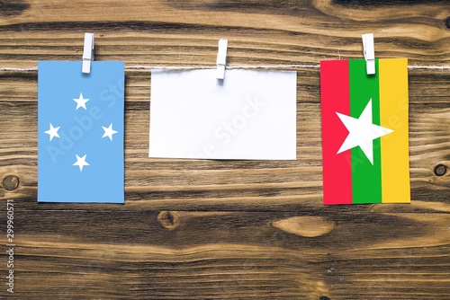 Hanging flags of Micronesia and Myanmar attached to rope with clothes pins with copy space on white note paper on wooden background.Diplomatic relations between countries. photo