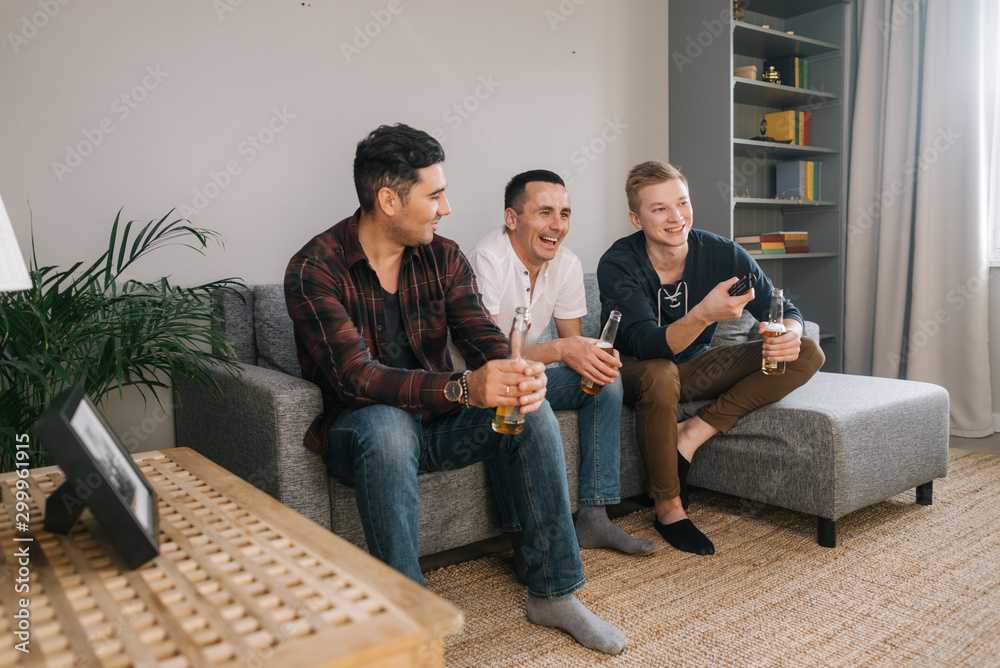 Cheerful young man watching TV. Group of friends spend time together behind the TV in the evening