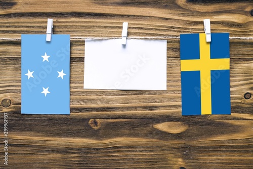 Hanging flags of Micronesia and Sweden attached to rope with clothes pins with copy space on white note paper on wooden background.Diplomatic relations between countries. photo