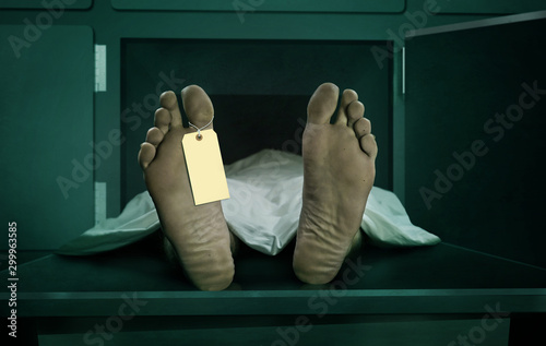 Male human body lying dead at morgue capsule with blank identification label . Close up foot of man cadaver covered with sheet having indentity tag on toe in death concept photo