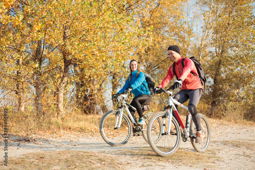 Smiling young couple enjoying relaxing mountain bike ride through the forest on a beautiful cold autumn morning. Active and healthy lifestyle
