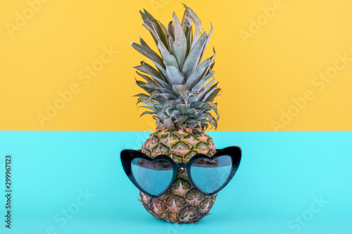 Funny attractive pineapple in stylish glasses on a yellow-blue background. Tropical summer vacation concept.