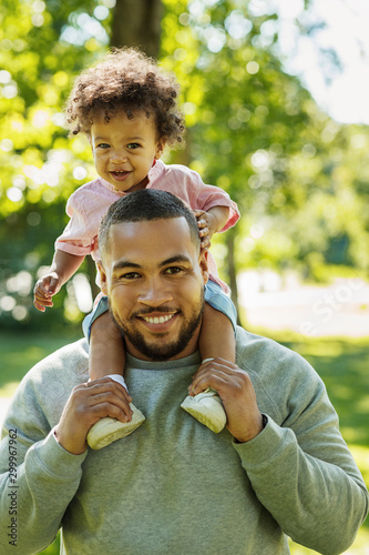 Young father carrying son on shoulders outdoors. Portrait of a young dad and his child in the park.