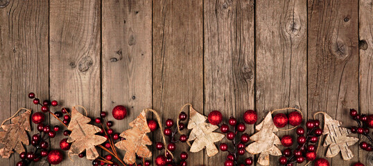 Christmas border banner with wood tree decorations and red baubles. Above view on an aged wood background.