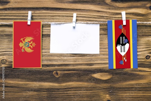 Hanging flags of Montenegro and Swaziland attached to rope with clothes pins with copy space on white note paper on wooden background.Diplomatic relations between countries.