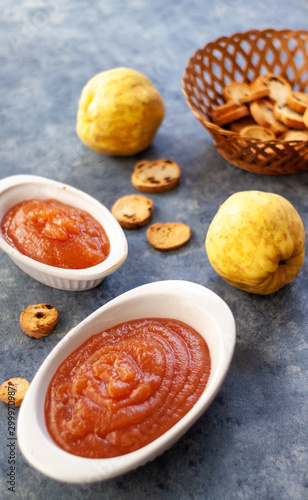 Homemade jelly quince in a white crockery containers with some quince fruits and little toasts to spread.