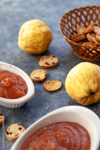Homemade jelly quince in a white crockery containers with some quince fruits and little toasts to spread.