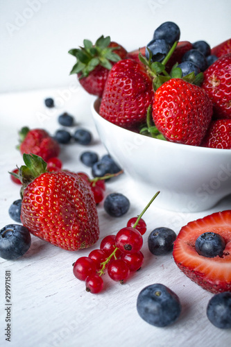 Fresh berries  strawberries  blueberries  red currant  in a white bowl on a white table  shallow depth of field