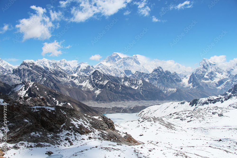 View of Everest mountain peak from the top of Renjo La Pass in Himalayas in sunny day. Everest rises above Lake Gokyo and the village of the same name. Clouds lies on the mountainside.