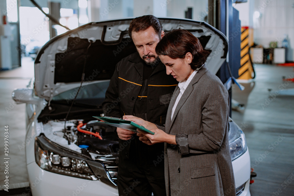 The manager from a auto service center have a conversation with the mature mechanic man they analyzing the problem of the car to write on the map