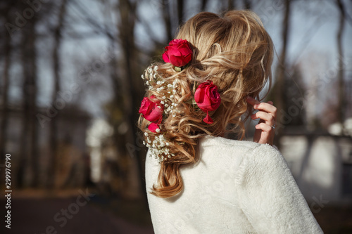 Elegant wedding hairstyle with roses and gypsophila on a blonde girl in autumn park, view from the back.