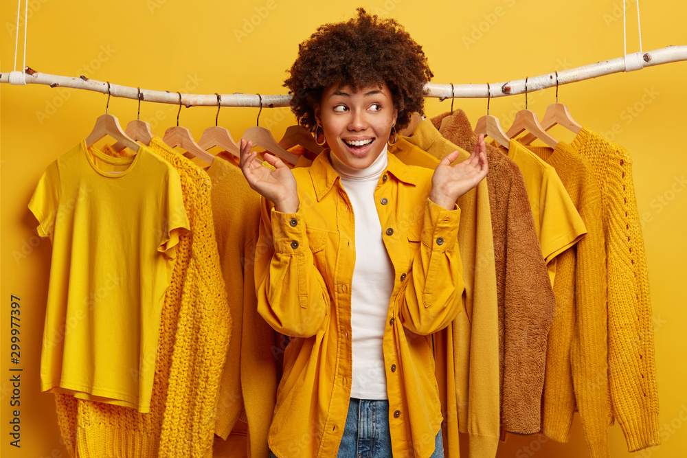 Happy unaware curly haired woman spreads palms with dreamy expression