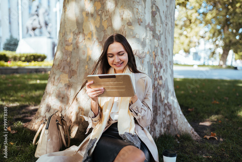 Foto pretender joyfully looks at a tablet pc while sitting under a tree in a park