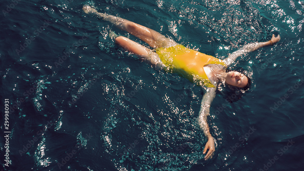 young woman in a one-piece yellow swimsuit floats on the surface of the water.