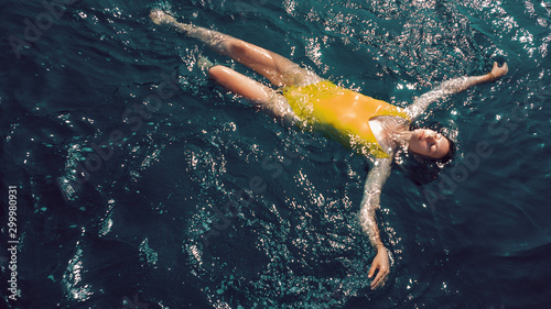 young woman in a one-piece yellow swimsuit floats on the surface of the water.