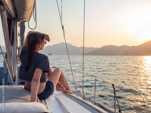 attractive young woman in a striped t-shirt enjoys the sunset on the deck of a sailing yacht. Girl yachtsman