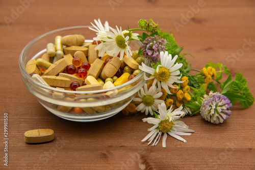 A bowl with various capsules and tablets, medicinal and aromatic herbs.