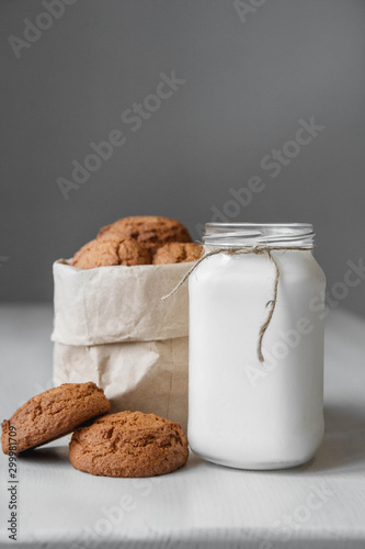Photo Milk in a glass jar and oatmeal cookies in a paper bag on a white table background