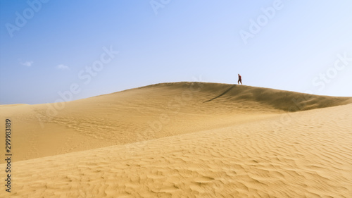 person in red walks on top of The great desert Dunas de Maspalomas in Gran Canary