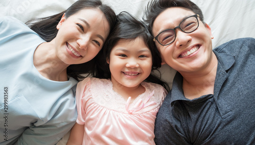 portrait of happy Asian family lying on bed and looking up and holding hands