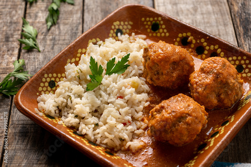 Mexican meatballs with red sauce and rice on wooden background