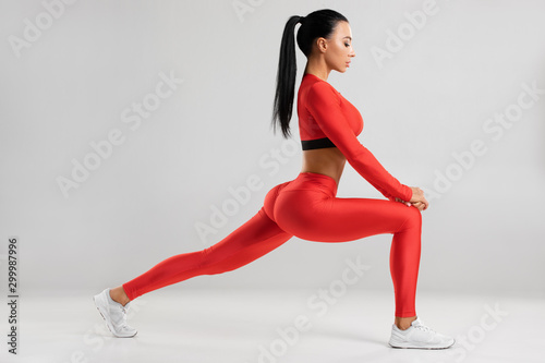 Fototapeta Naklejka Na Ścianę i Meble -  Fitness woman doing lunges exercises for leg muscle workout training. Active girl doing front forward one leg step lunge exercise, on the gray background
