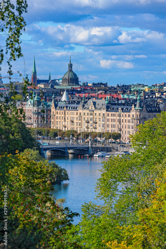 High point view to Stockholm streets from Djurgarden island across the river at sunny autumn day with fall lush foliage trees at foreground.