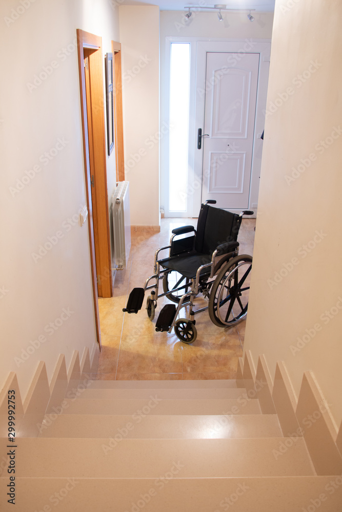 A wheelchair in front of a staircase in a house - obrazy, fototapety, plakaty 