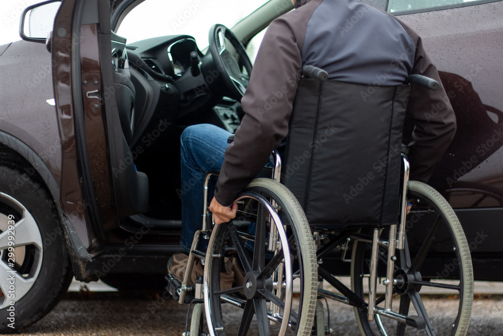 A man in a wheelchair trying to get into the driver's seat of a car A man in a wheelchair trying to get into the driver's seat of a car