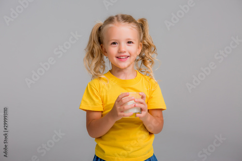 little blonde girl in yellow tank top holding a glass of milk on a light background, space for text