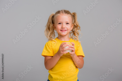 little blonde girl in yellow tank top holding a glass of milk on a light background, space for text