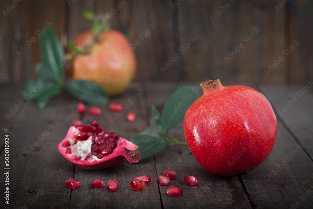 Fresh pomegranates with leaves on wooden background.Two ripe, juicy pomegranates, one cut. Fresh pomegranates with leaves on wooden background.Two ripe, juicy pomegranates, one cut.