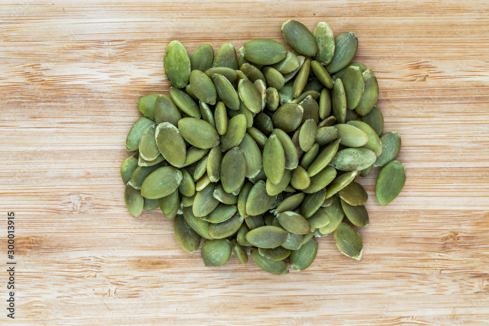 Huskless pumpkin seeds lie in a heap in the center on a brown wooden surface, top view Huskless pumpkin seeds lie in a heap in the center on a brown wooden surface, top view