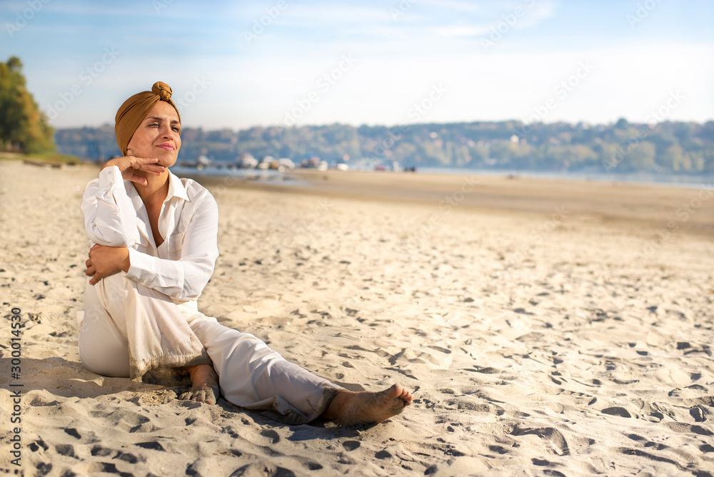 Elegant woman in white robes with turban sitting on the beach