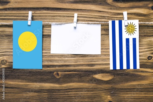 Hanging flags of Palau and Uruguay attached to rope with clothes pins with copy space on white note paper on wooden background.Diplomatic relations between countries. photo