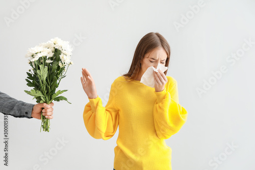 Young woman with allergy refusing to take flowers from man on light background photo