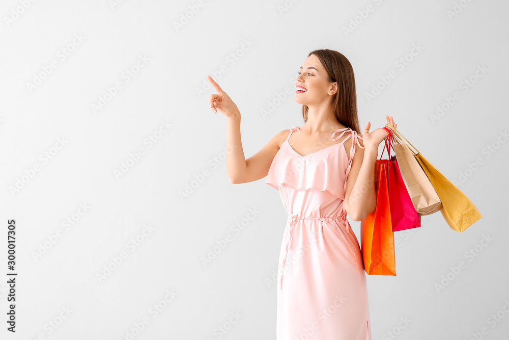 Beautiful young woman with shopping bags pointing at something on light background Beautiful young woman with shopping bags pointing at something on light background