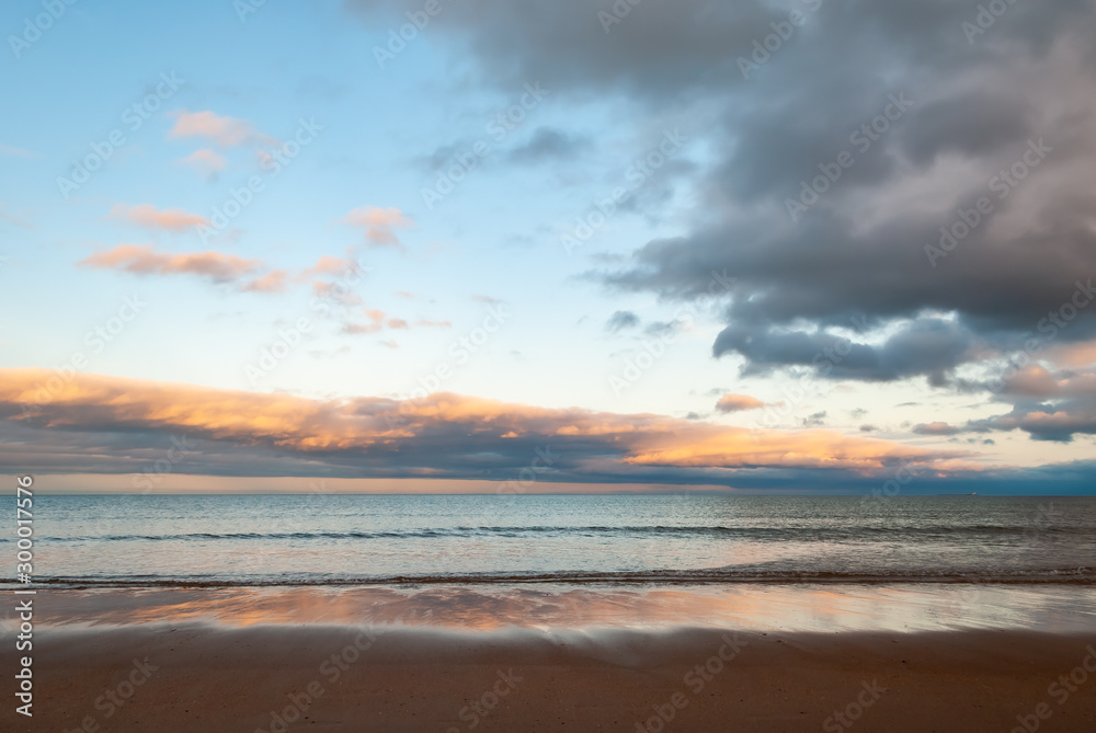 Dramatic sky over the sea as waves gently lap onto the beach in the golden light of the setting sun