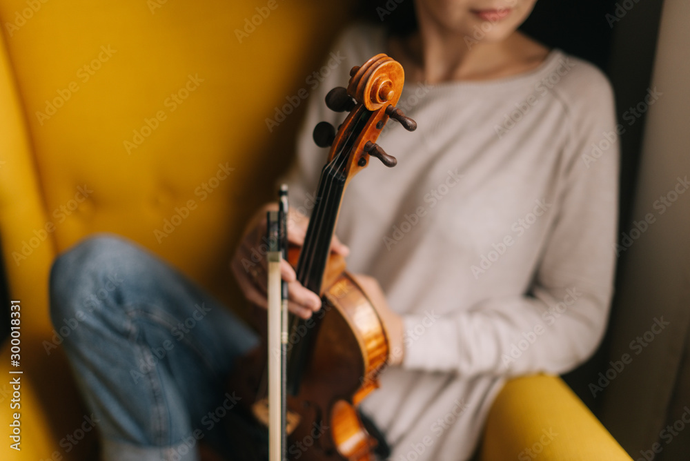 Beautiful young woman musician posing with a violin in a soft chair
